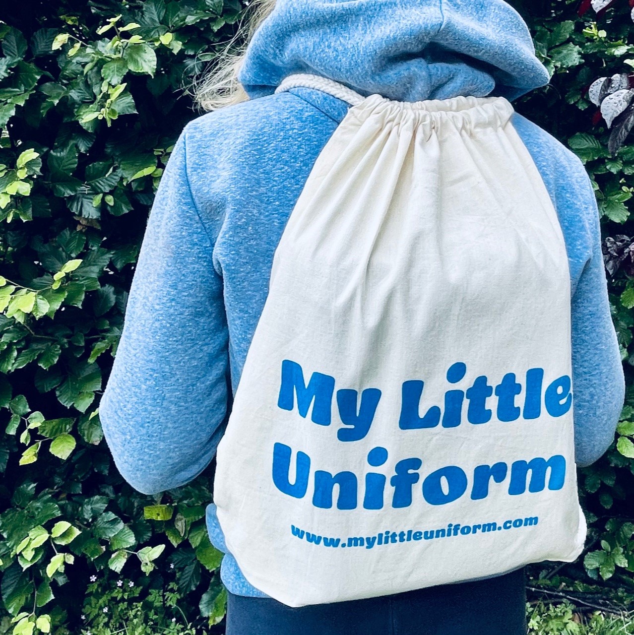 a child wearing a branded cotton drawstring backpack with My Little Uniform printed in blue lettering